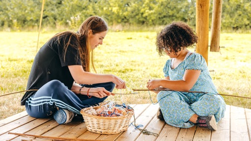A woman and girl having a go at wrapping wool around a willow stick outside